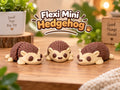 Three cute Flexi Mini Hedgehog 3D-printed toys in cream and brown, displayed on a warm wooden tabletop with plants and a cozy natural background. Wigglenest collectible articulated mini toys designed for playful display and gifting
