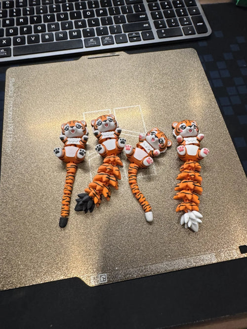 Cute articulated 3D printed tiger toys with flexible tails in orange, white, and black PLA, handmade by WiggleNest Malaysia.