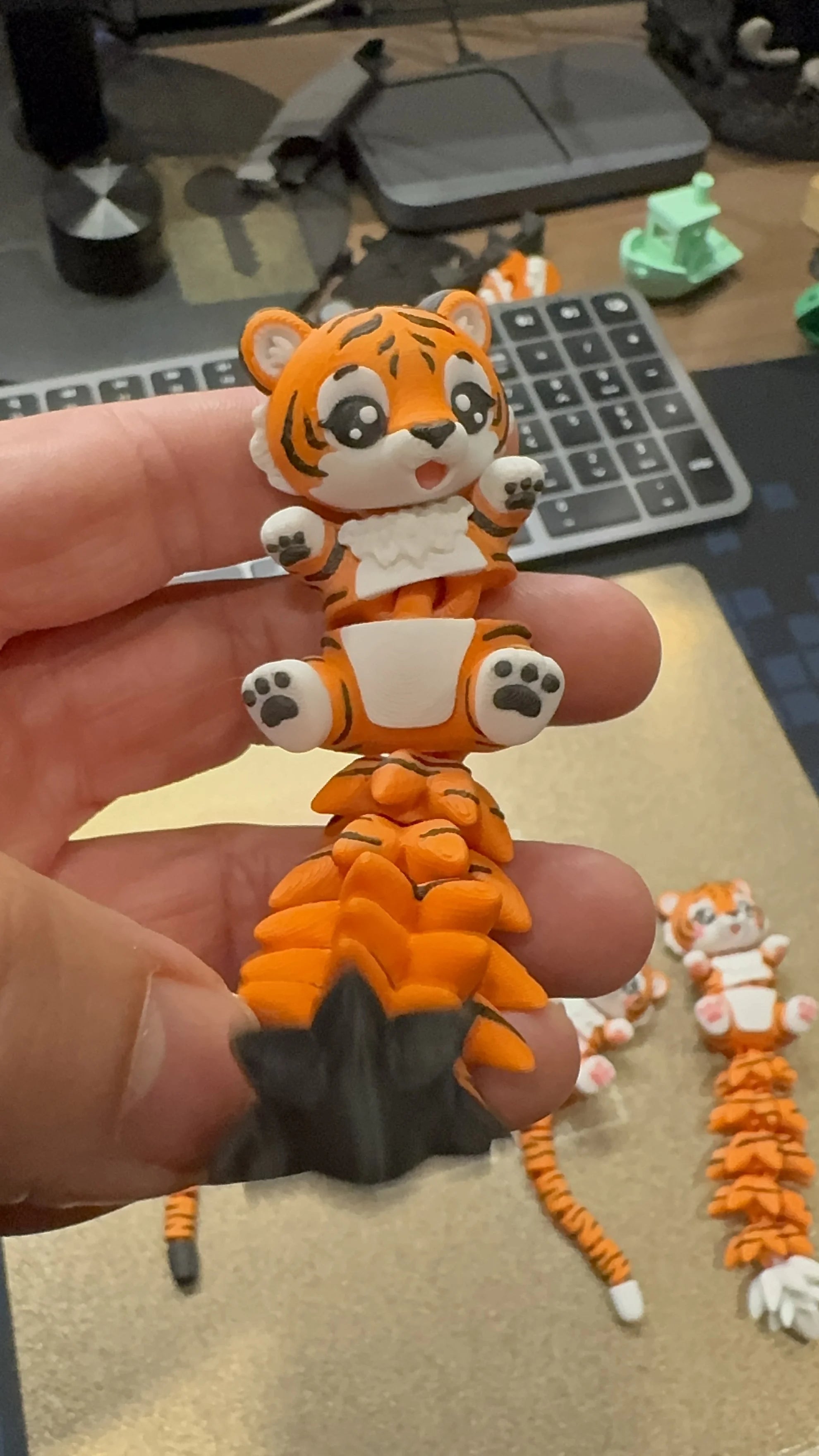 Close-up of a cute articulated 3D printed tiger toy with a flexible segmented tail, held in hand, designed by WiggleNest.