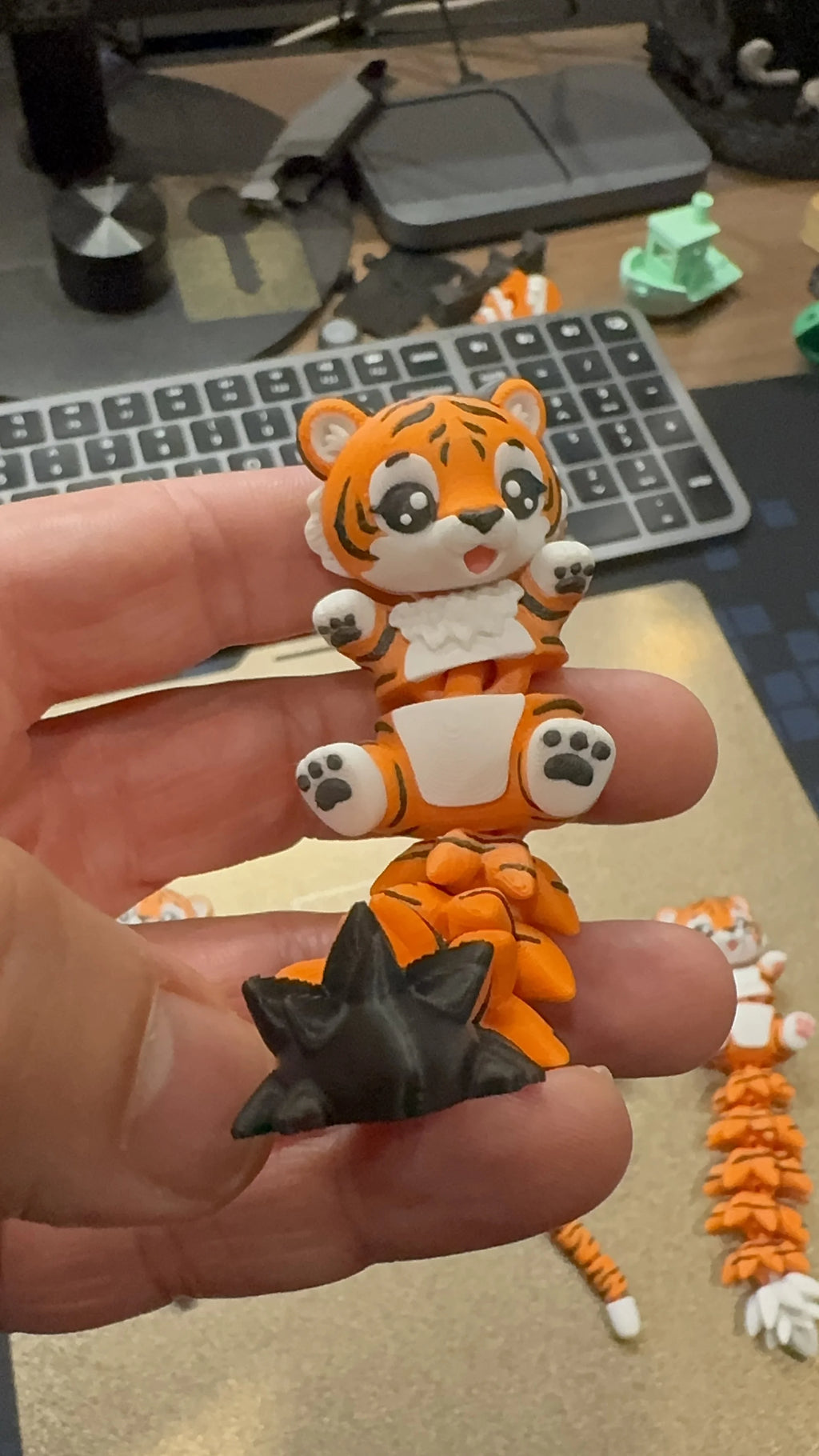 Close-up of a cute articulated 3D printed tiger toy with a flexible segmented tail, held in hand, designed by WiggleNest.