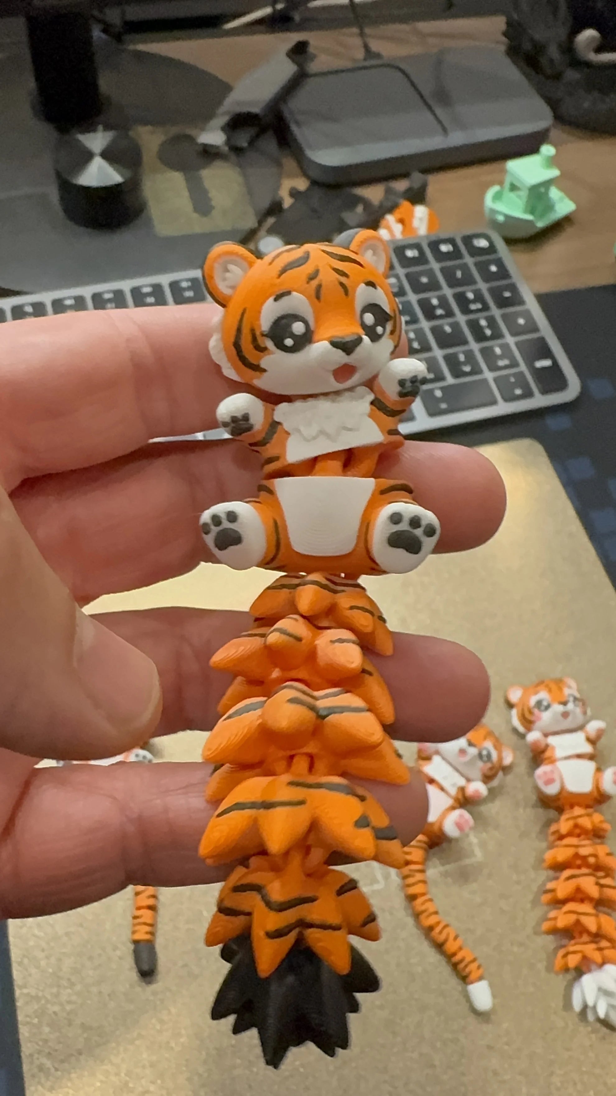 Close-up of a cute articulated 3D printed tiger toy with a flexible segmented tail, held in hand, designed by WiggleNest.
