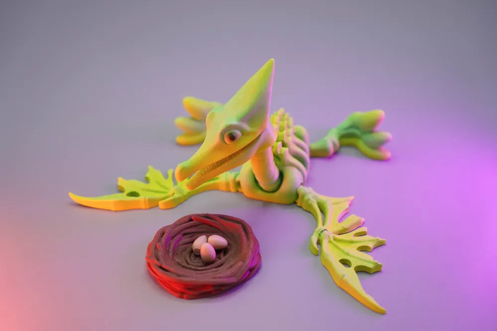 3D printed articulated pterosaur skeleton toy in bright green beside a detailed nest with eggs, displayed under colourful studio lighting.